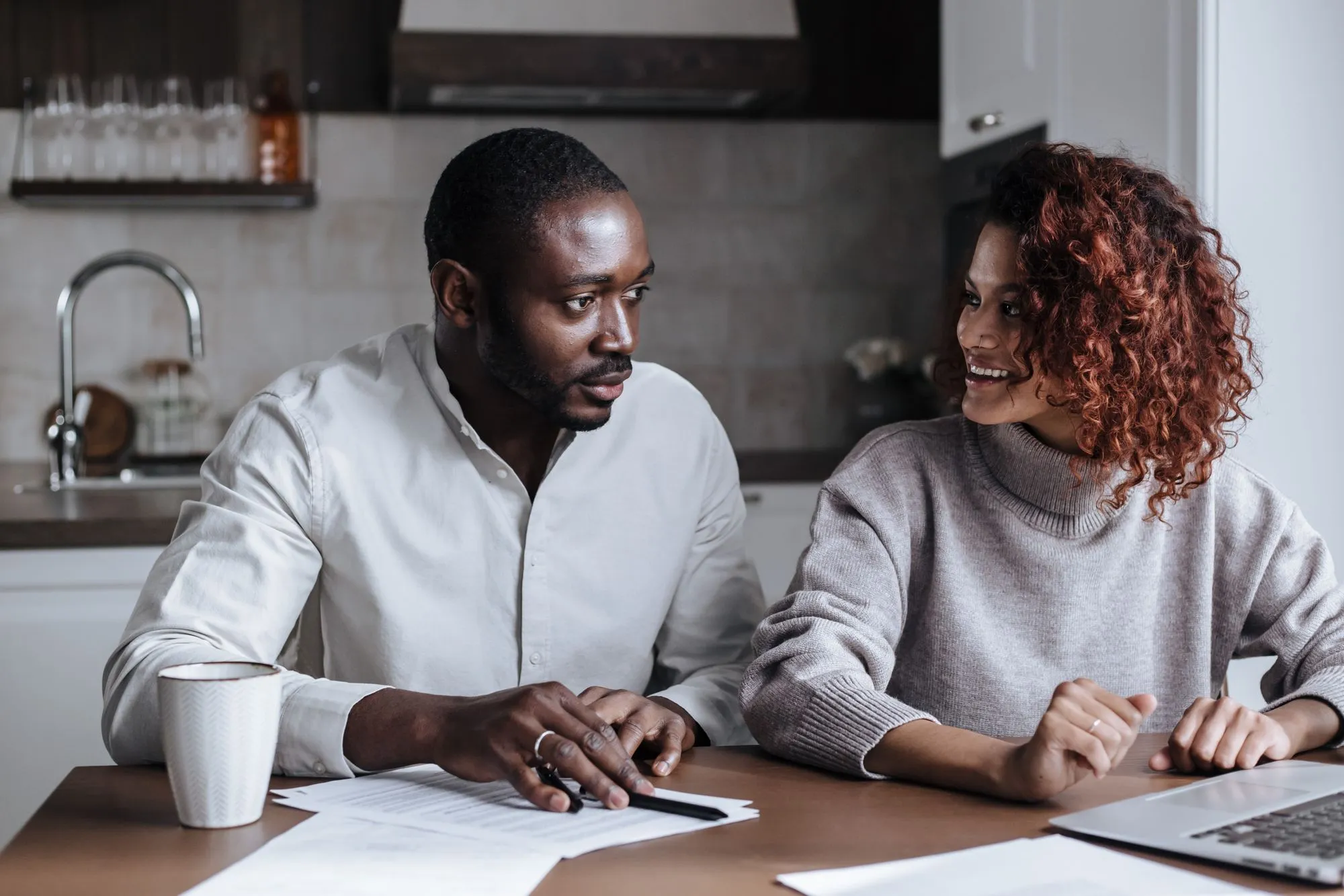 Un couple compare ses assurances à la maison, documents et ordinateur portable sur la table.
